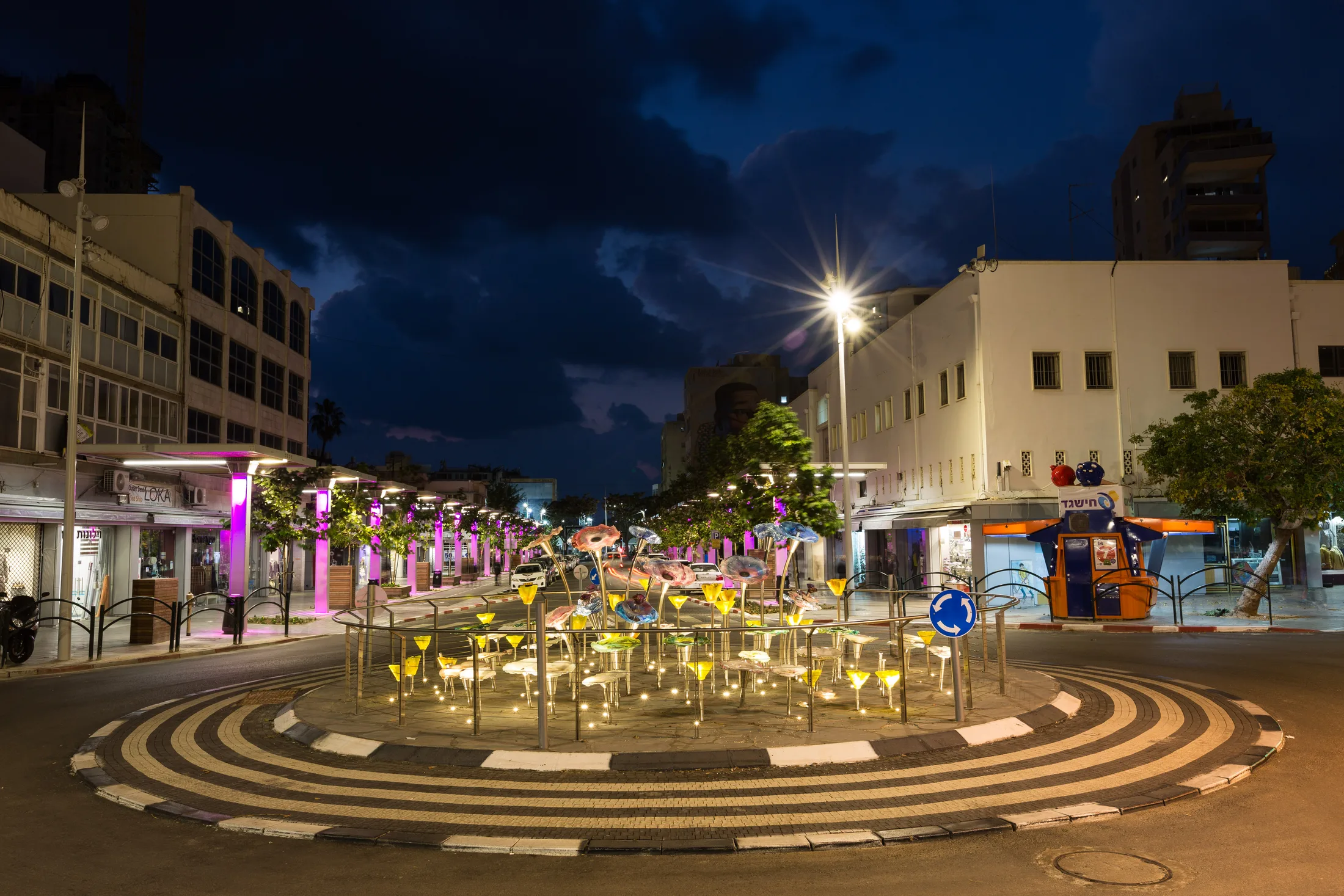 A plaza with the lit flower installation and colorful lighting at night