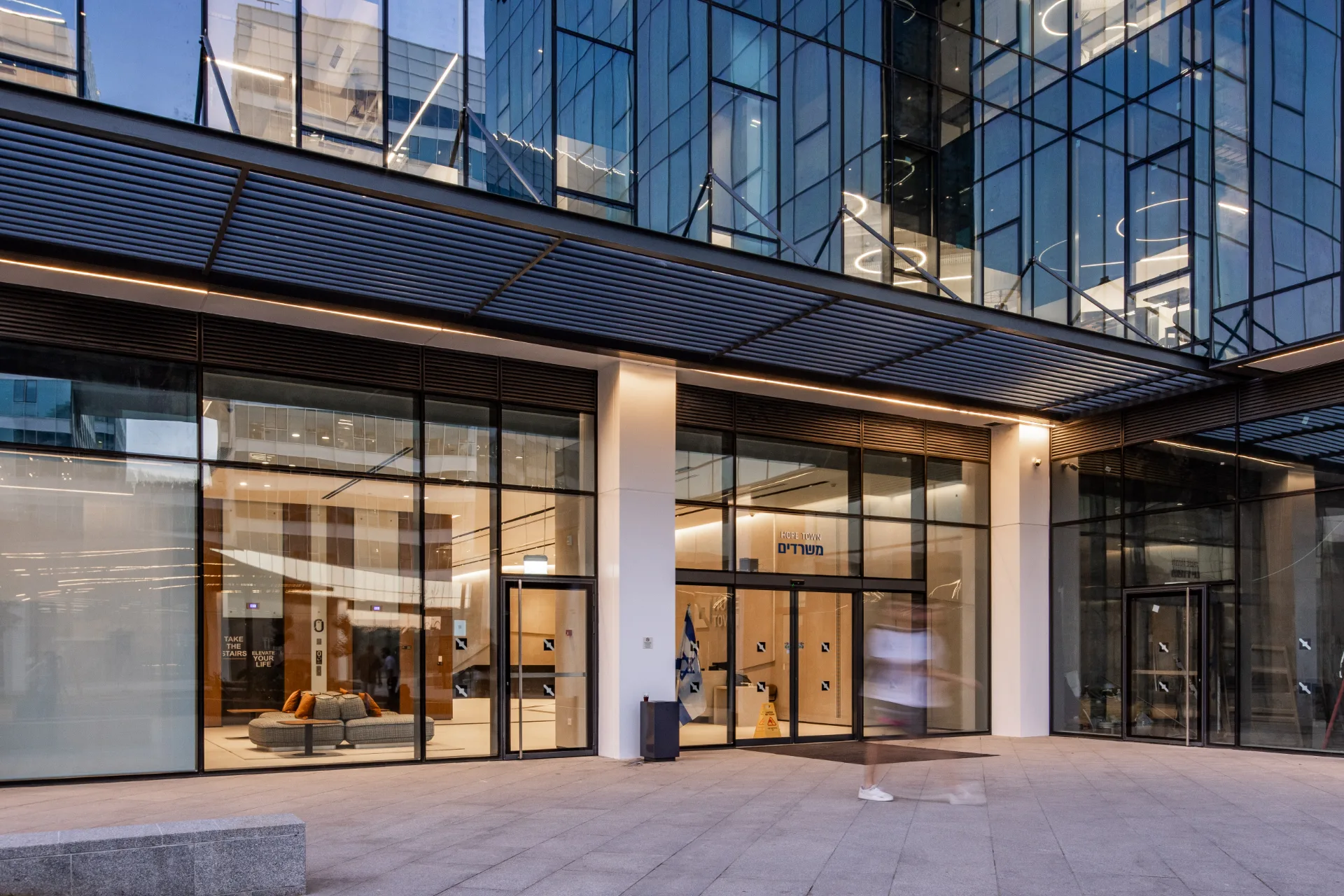 Building facade and lit lobby along the plaza at dusk