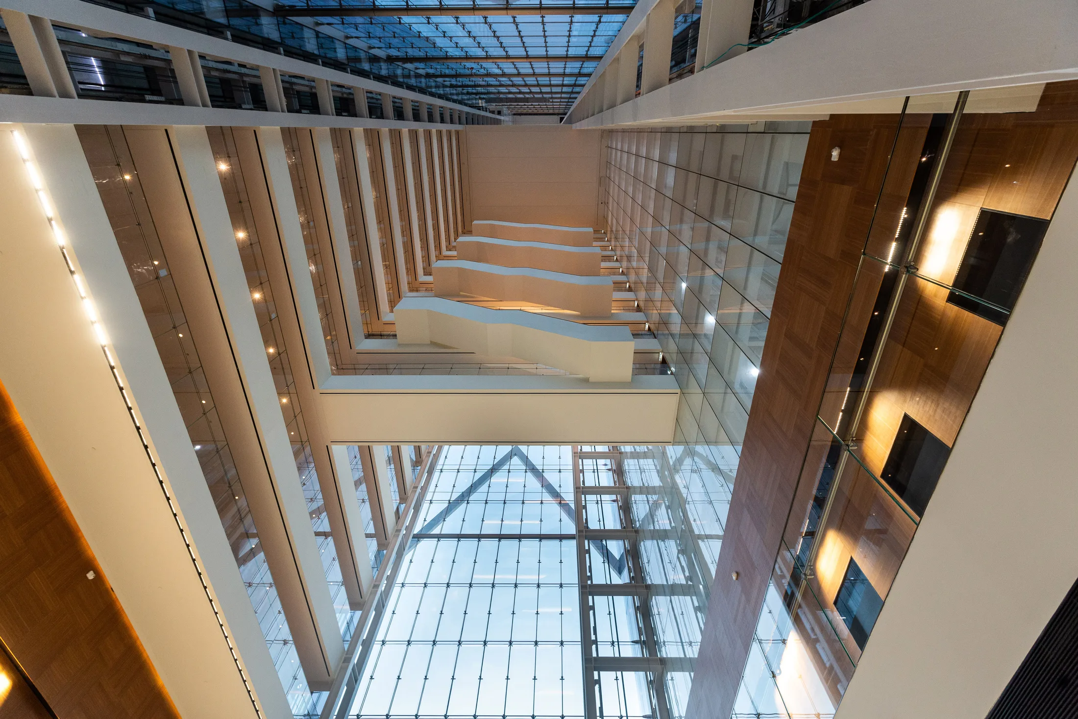 An upward view of the atrium with walkway bridges, perimeter cove lighting, and a glass roof