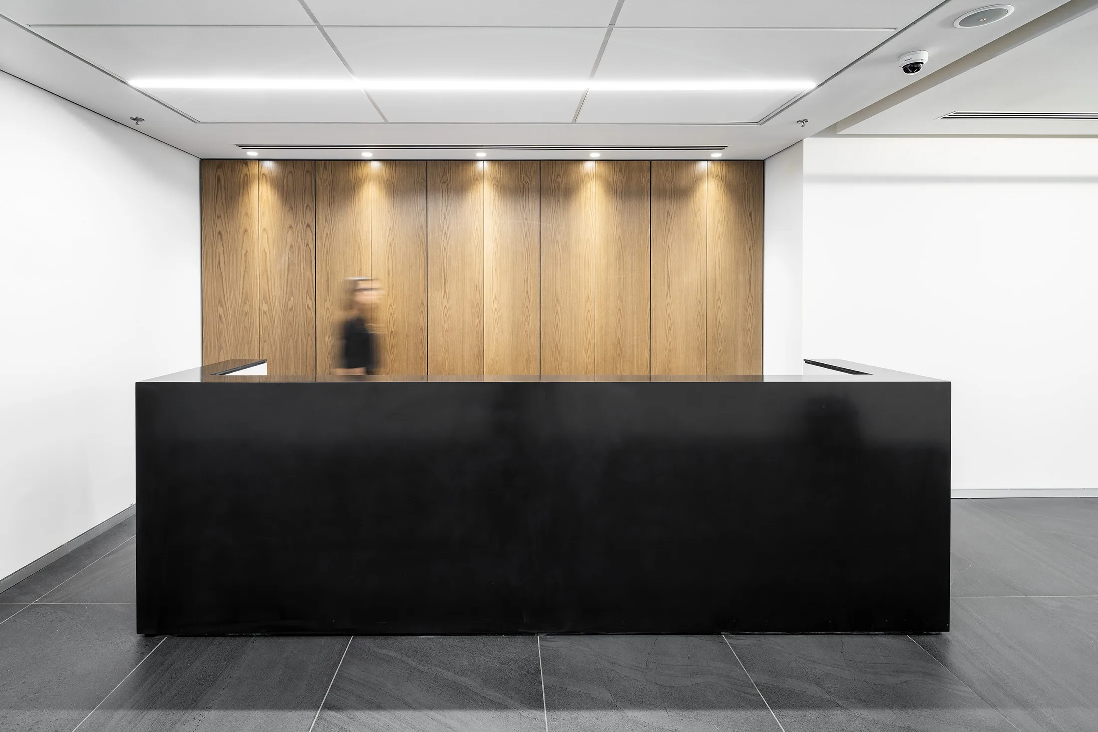 A dark reception desk against a wood wall washed with light