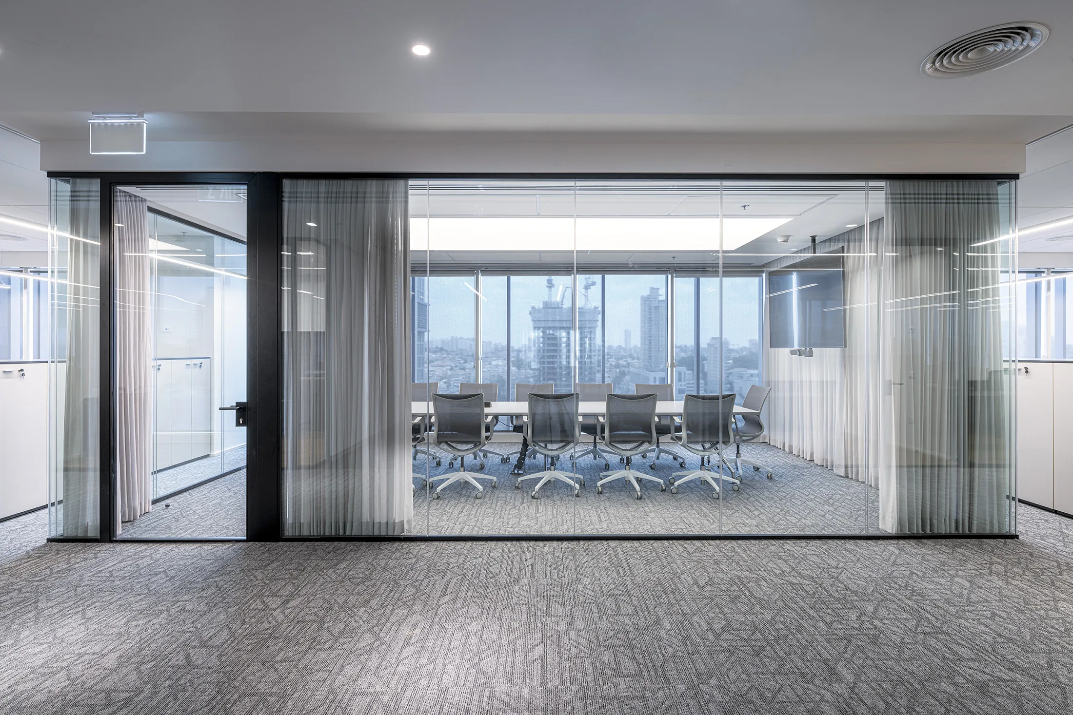 A glass-walled meeting room with sheer curtains and a city view