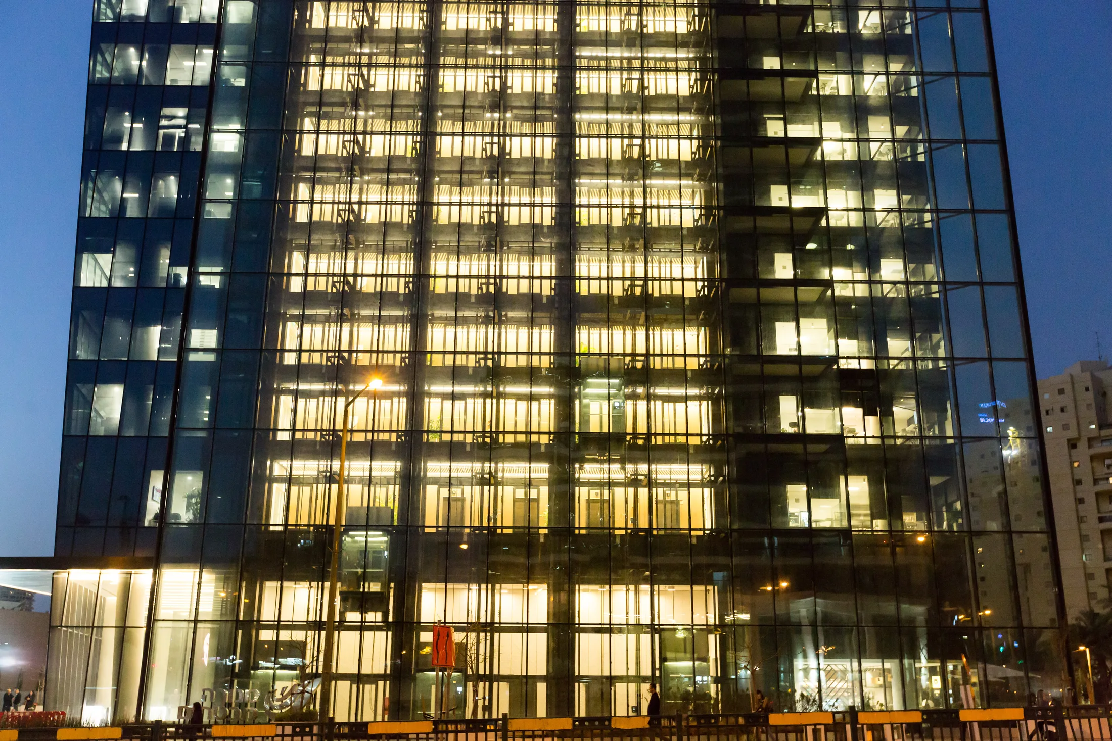Warm-lit office floors reading through the dark glass facade