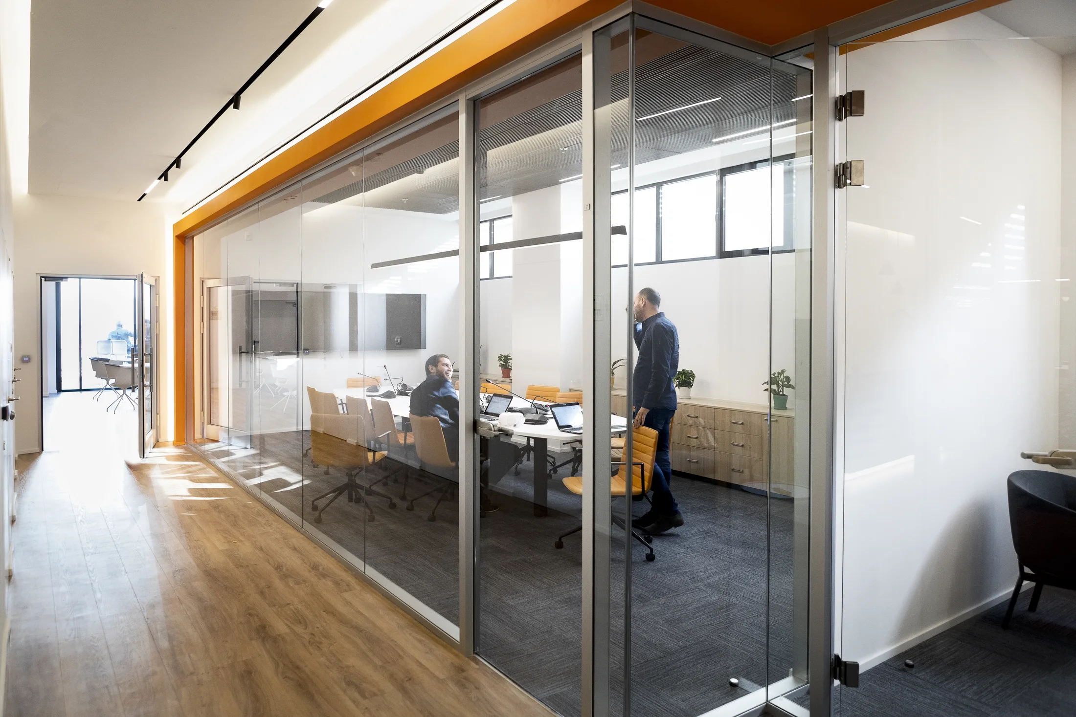 A glazed meeting room with an orange accent and track lighting