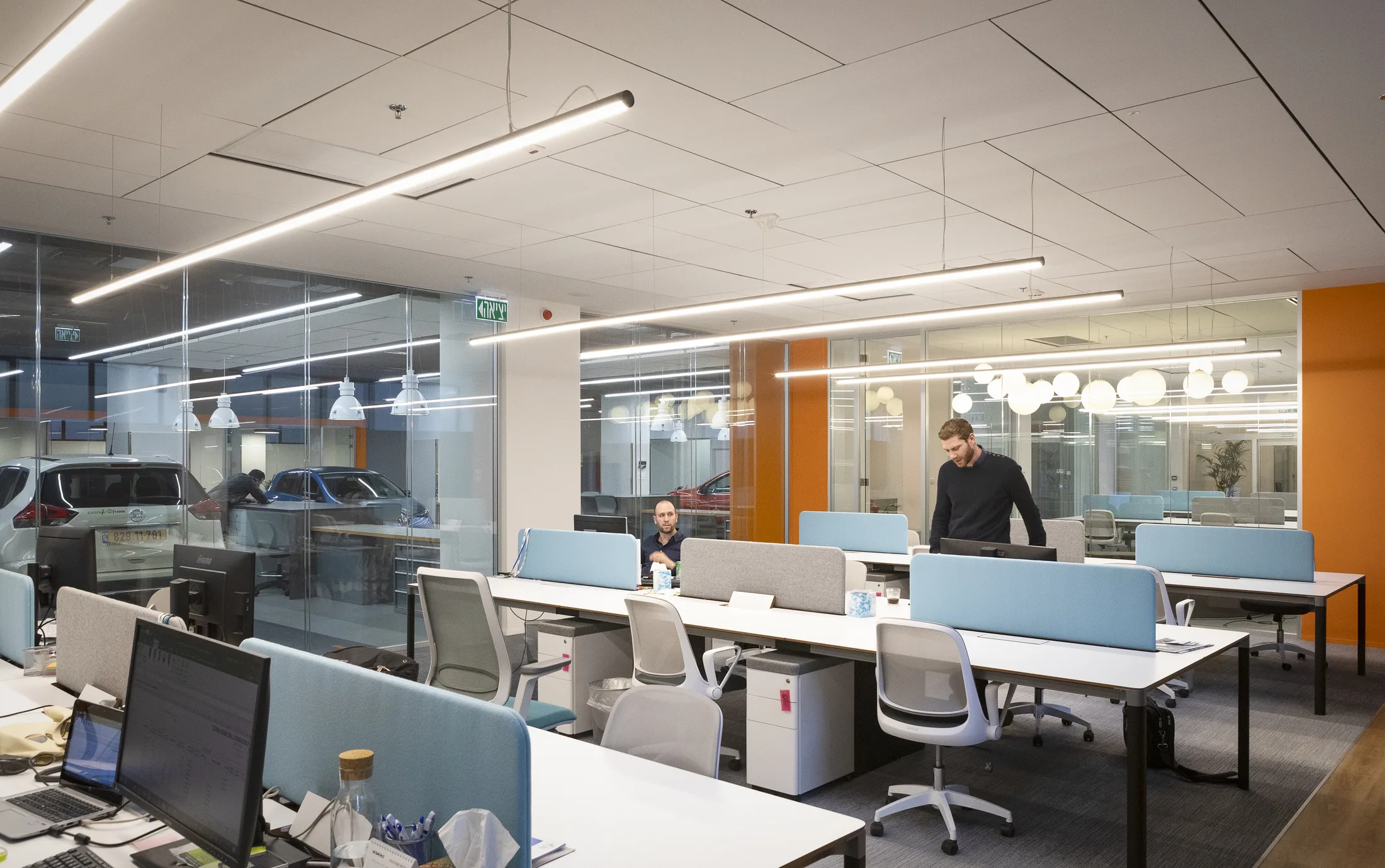 The open office with suspended linear lighting and cars beyond the glass
