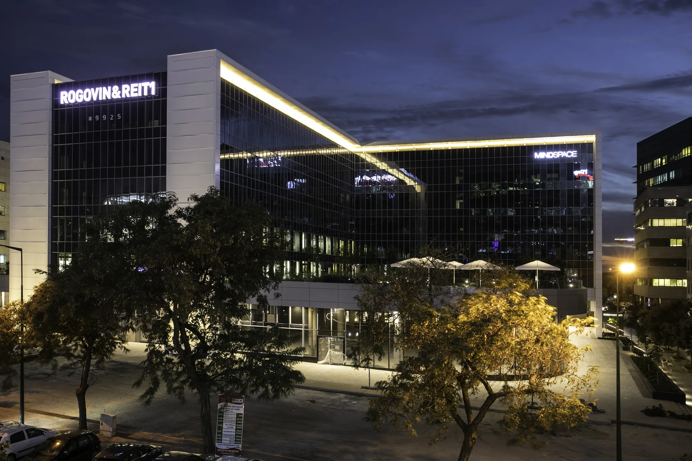 A wide view of the lit chevron facade and the patio at twilight