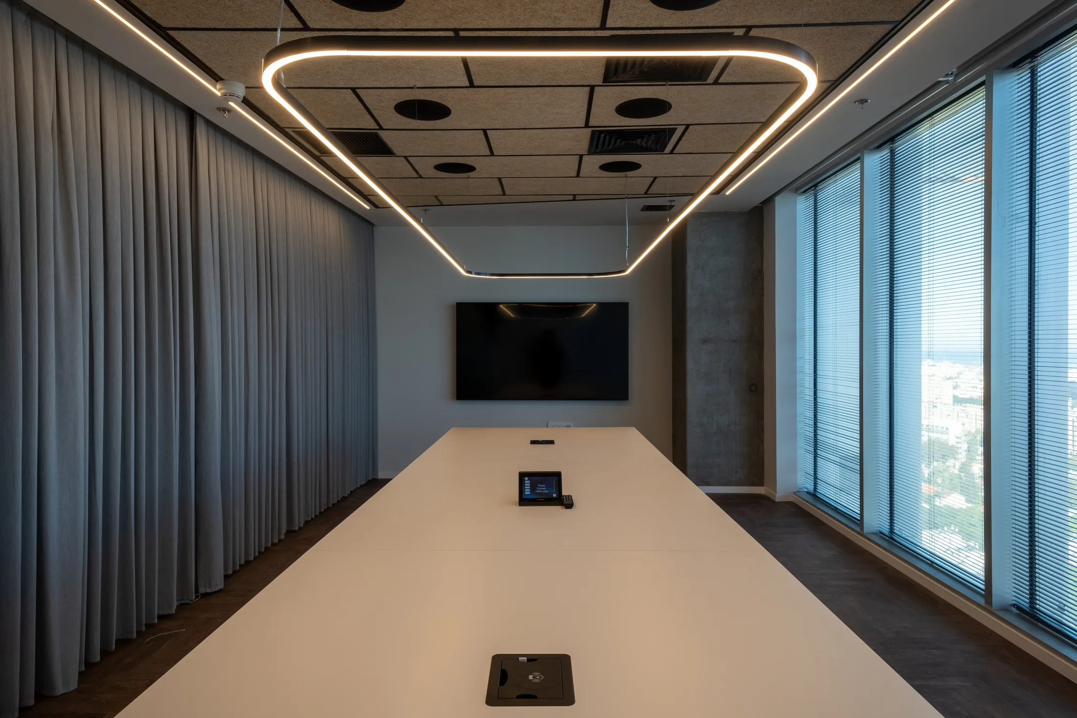 A boardroom with a suspended elongated ring luminaire over the table