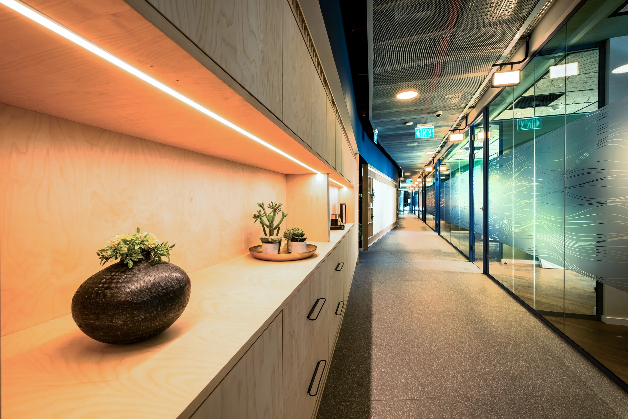 A corridor with warm cove lighting in the wood joinery and glass fronts