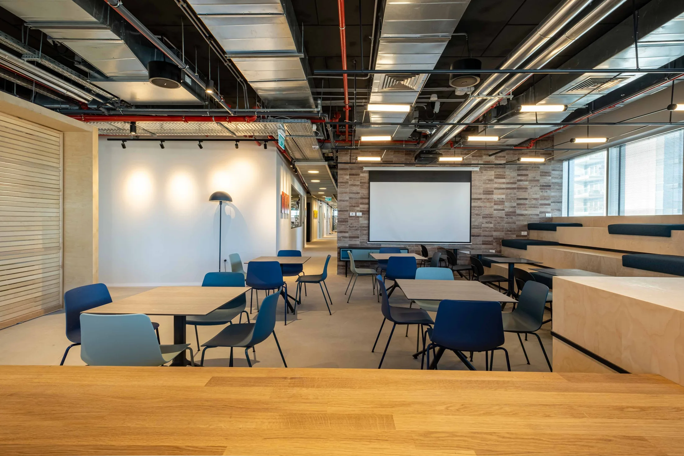 A café with tiered seating, pendant lights, and blue chairs