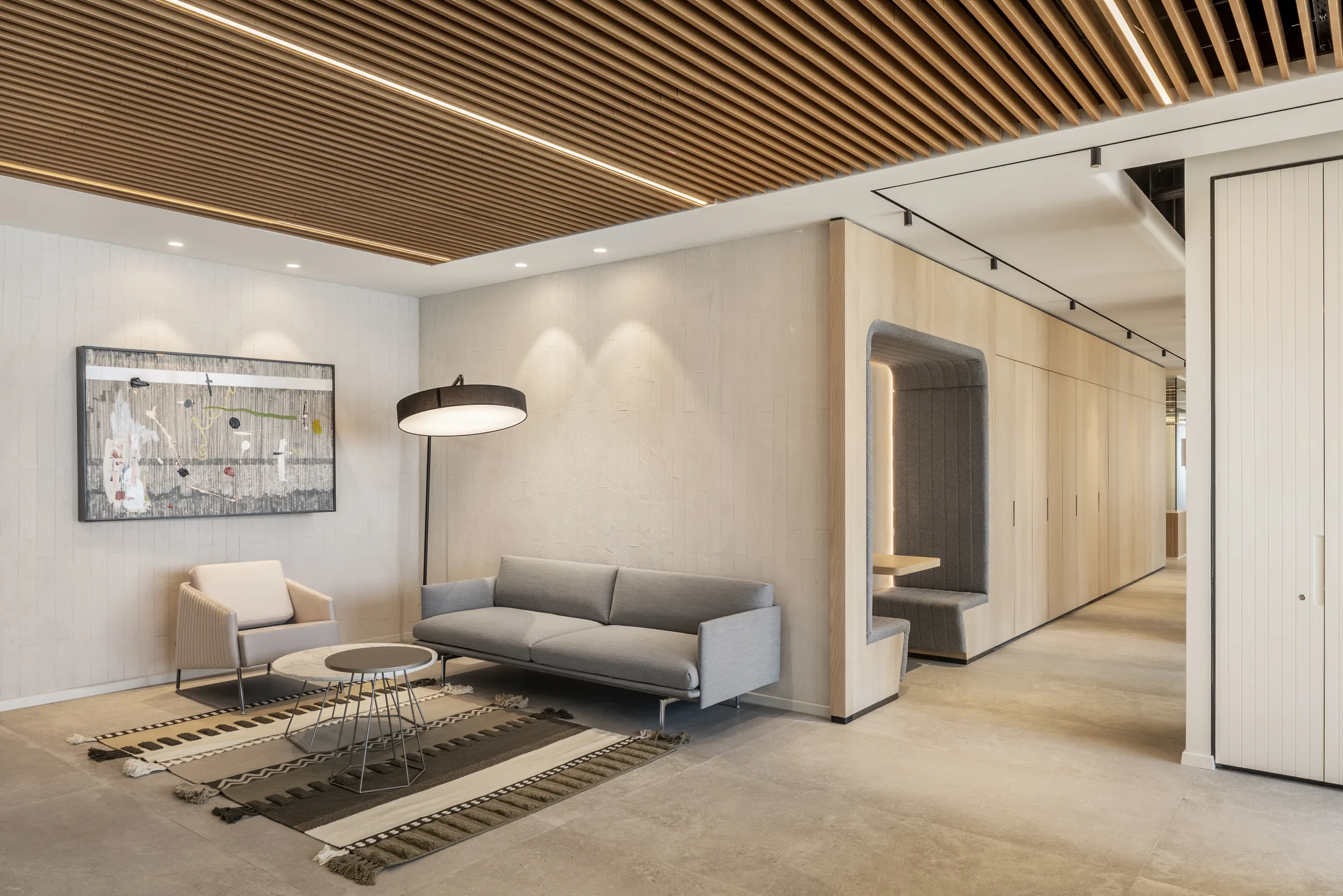 A lounge with a floor lamp, a lit slat ceiling, and a glowing seating nook