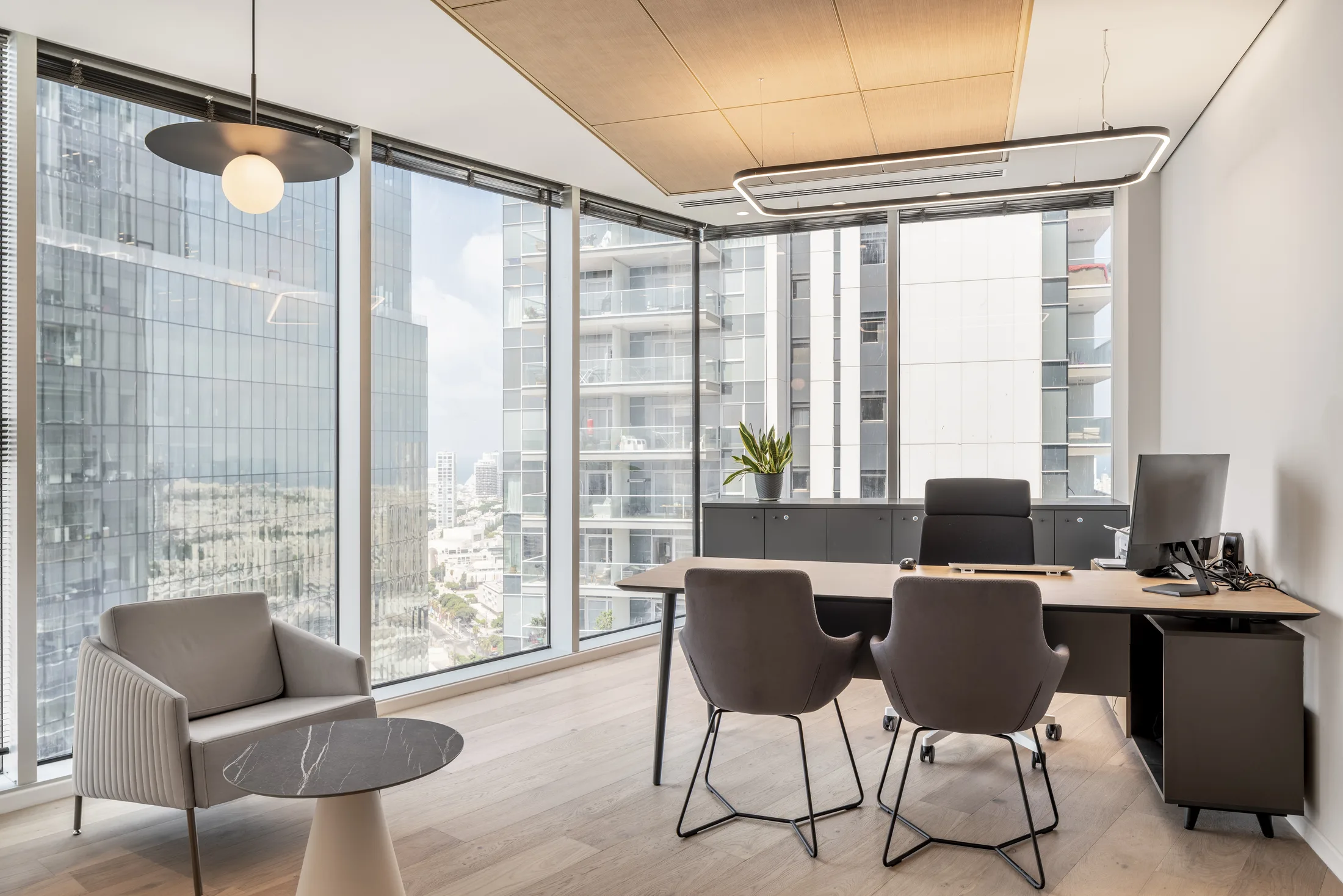 A corner office with a suspended rectangular frame luminaire and a globe pendant facing the view