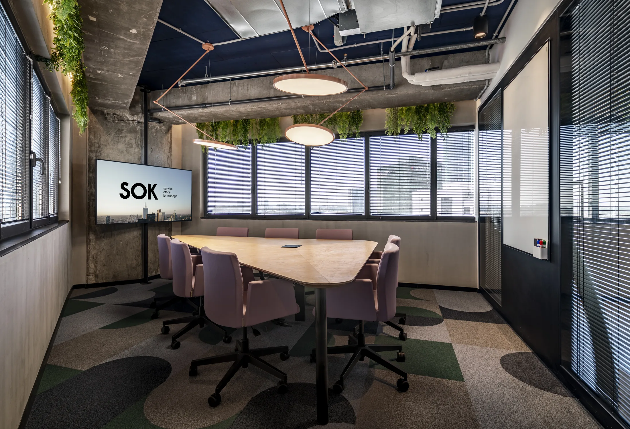 A meeting room with disc pendants, greenery, and a city view