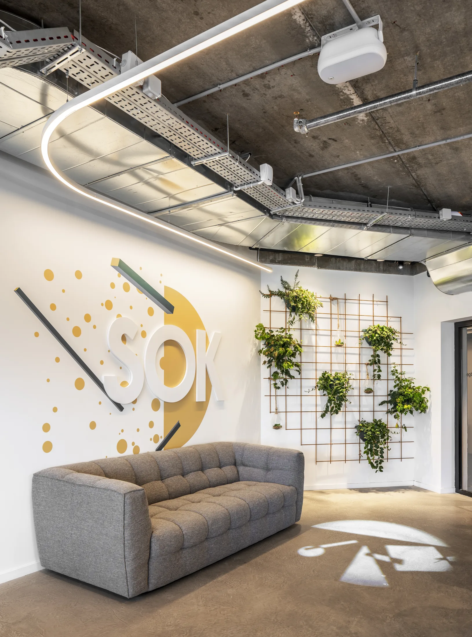 A lounge with the SOK logo, a plant wall, and a curved light line