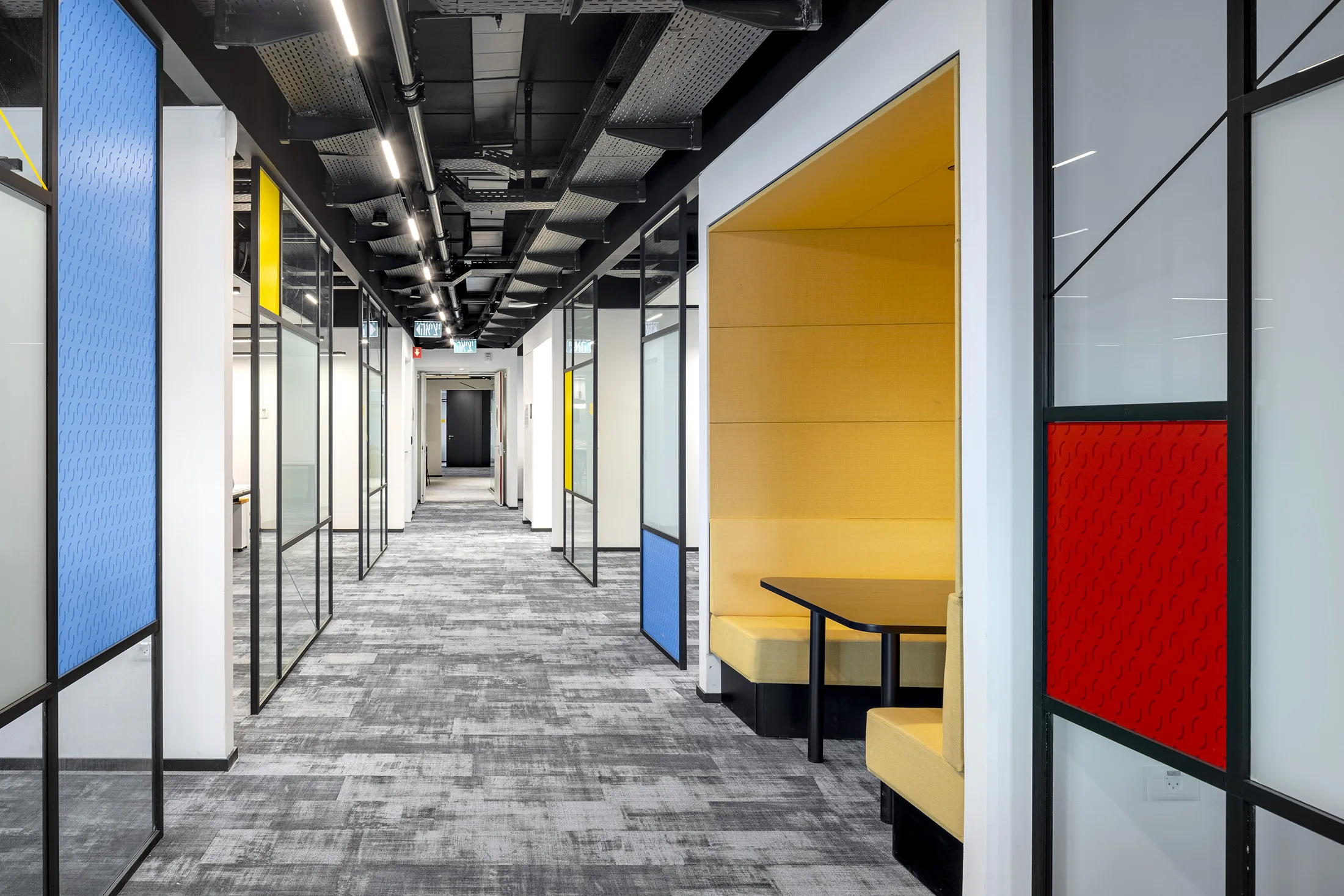 A corridor with primary-colored glass partitions and an acoustic seating booth