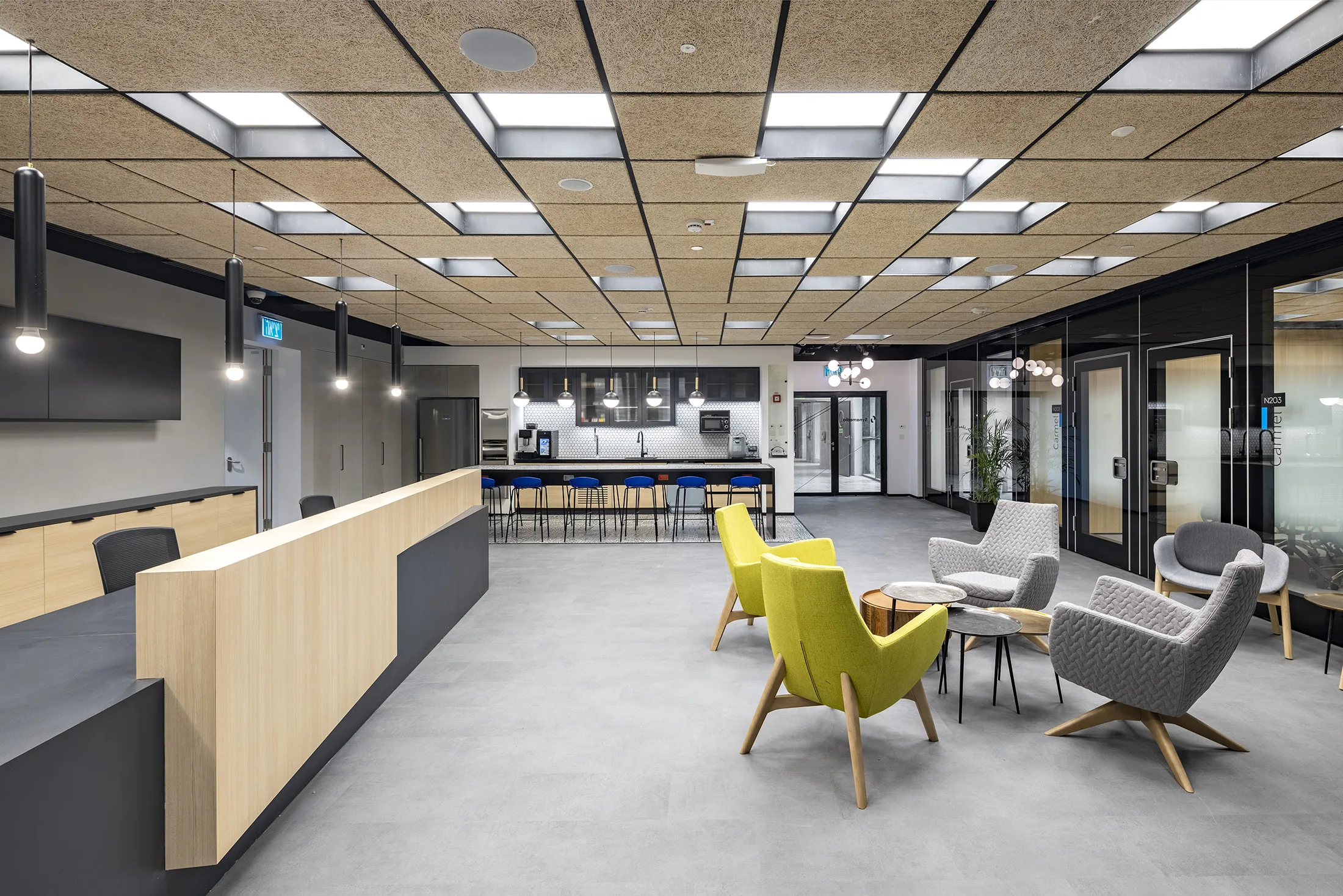 A lounge and kitchen with a lit wood acoustic ceiling and yellow armchairs
