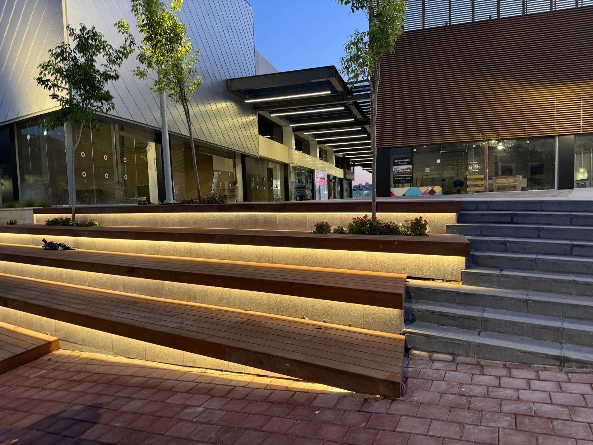 Illuminated stepped seating and storefronts beneath the timber soffit