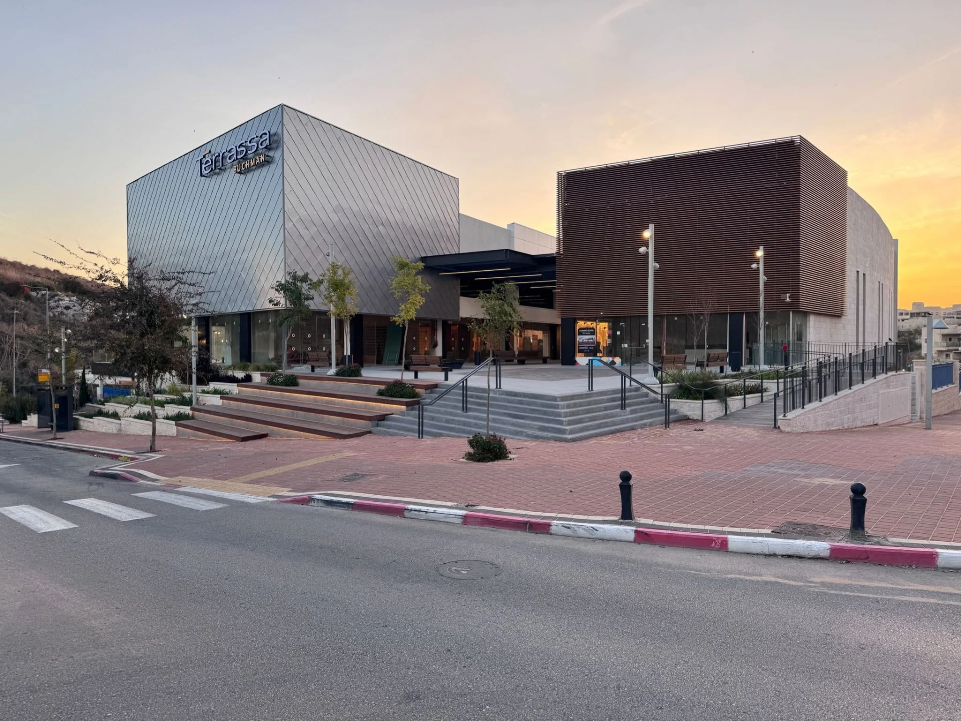 Perforated-metal and timber facades above the plaza at sunset