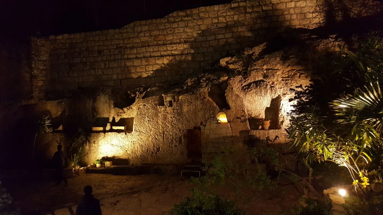 The lit tomb and rock face seen across the garden