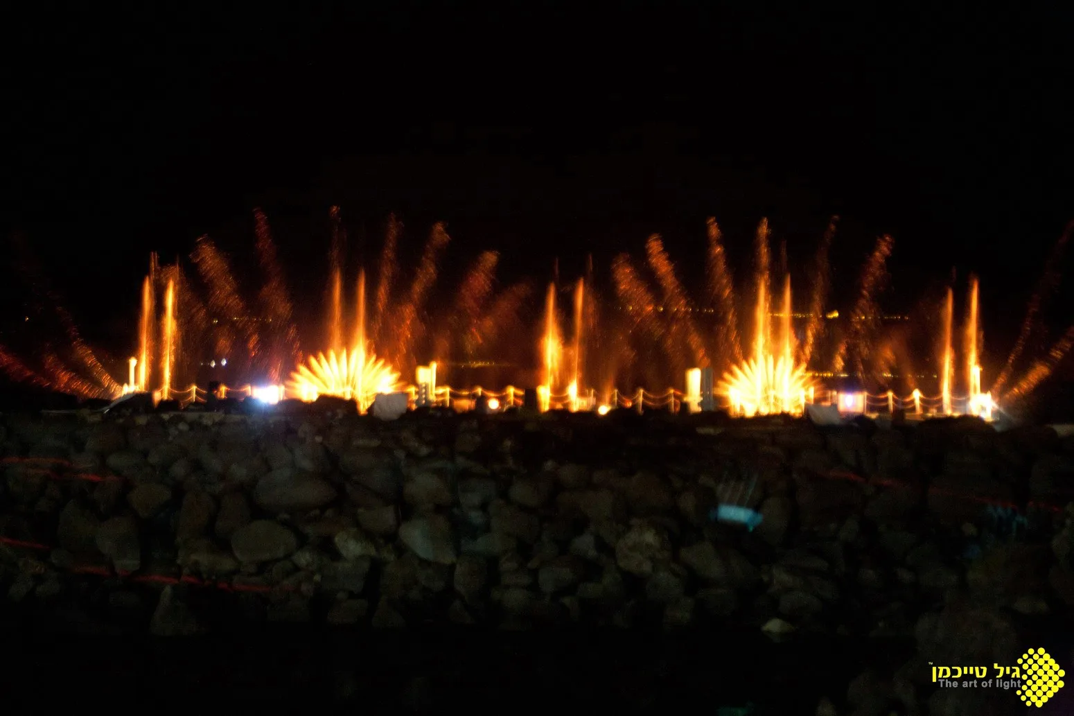 Amber water jets fanning across the night water