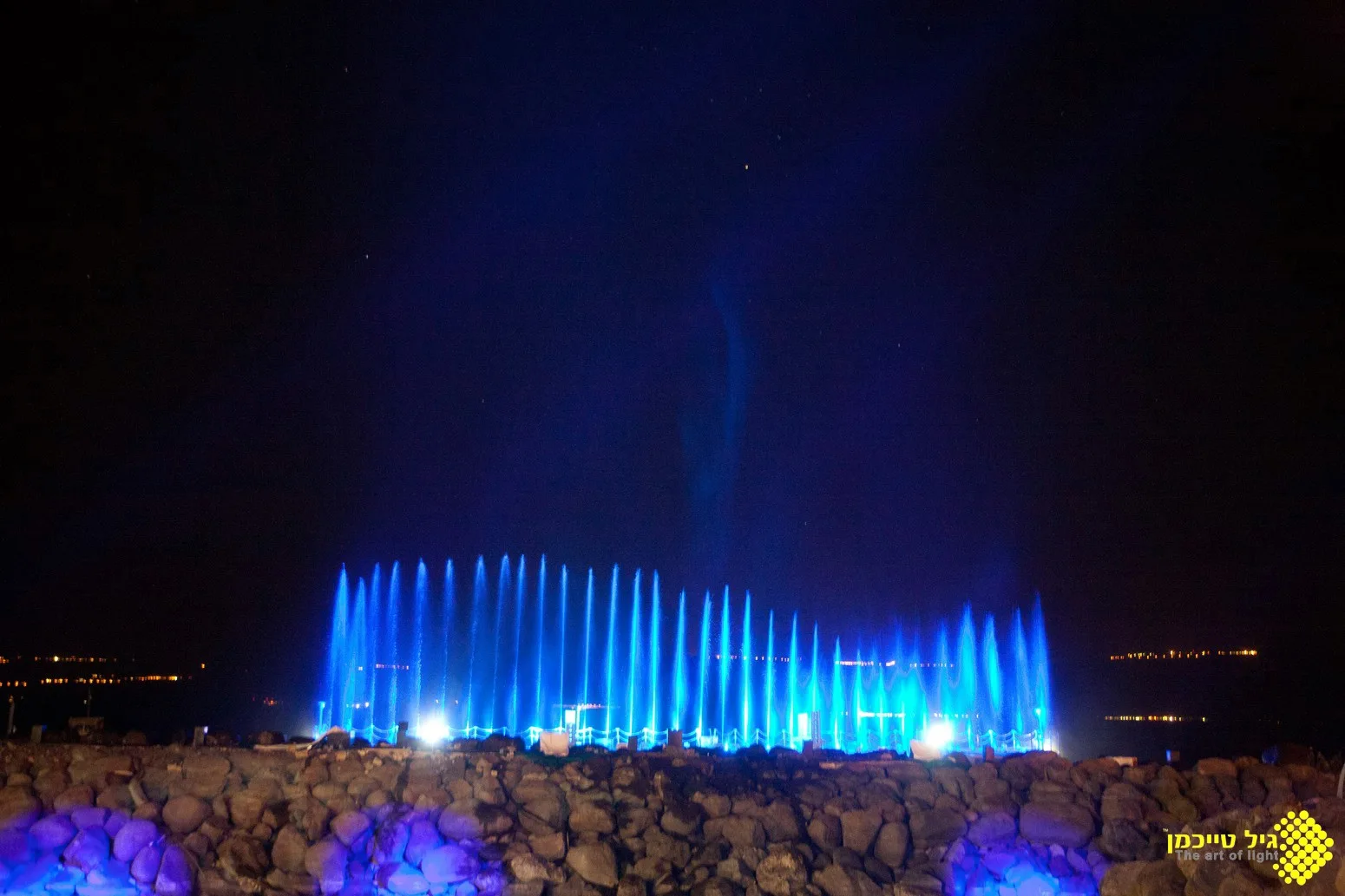 A long row of blue-lit fountain jets on the Sea of Galilee