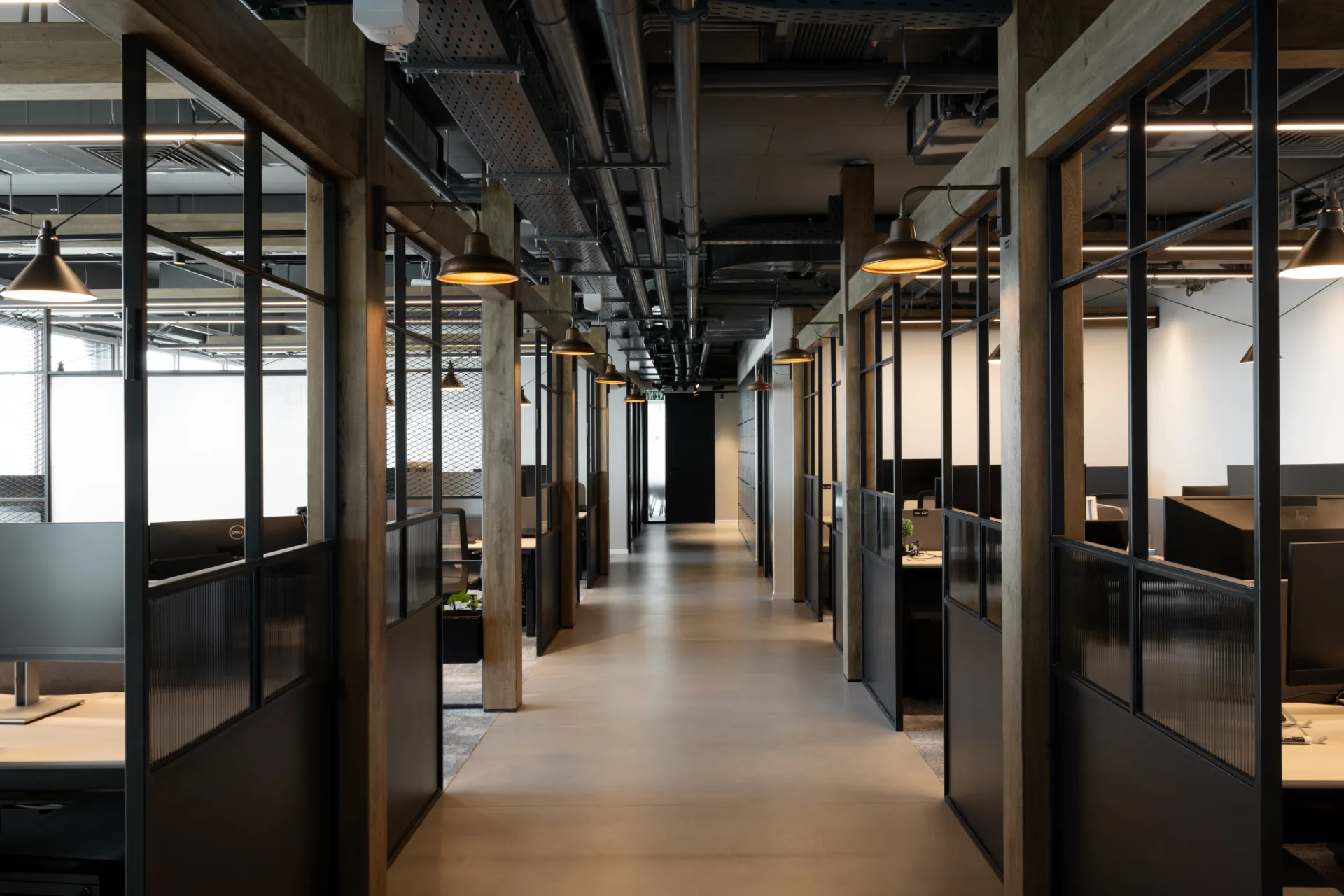 Corridor of glazed team rooms lit by warm pendants