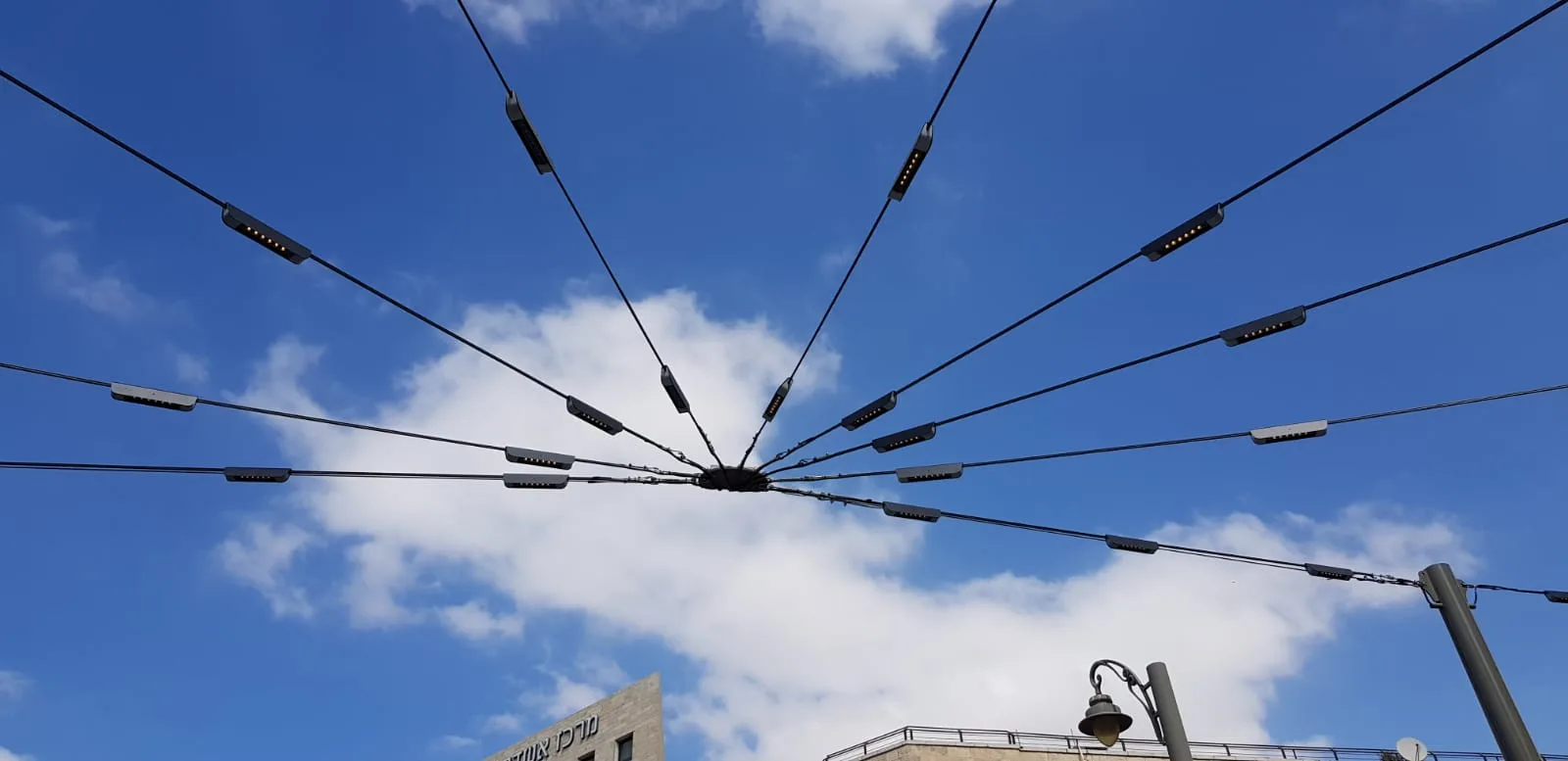 A daytime view up at the radial fan of linear LED luminaires cabled over the square